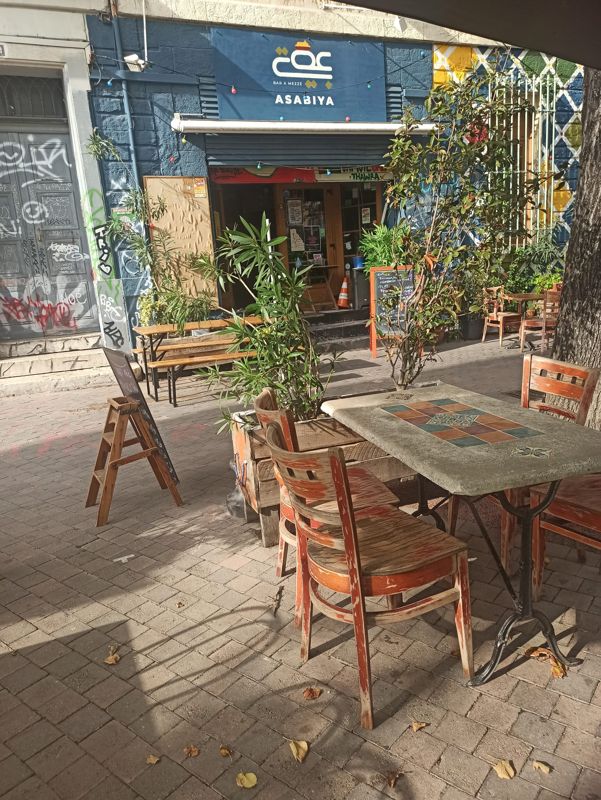 La terrasse d’Asabiya, ses tables en bois et ses plantes, devant la façade bleue