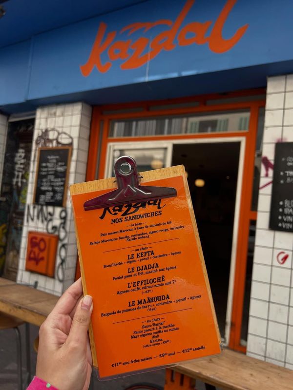La carte orange de Kazdal tenue devant la devanture, rue des Trois-Mages