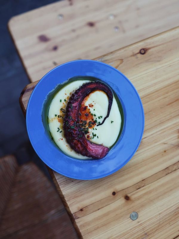 Une assiette bleue de poulpe sur une crème blanche, posée sur une table en bois