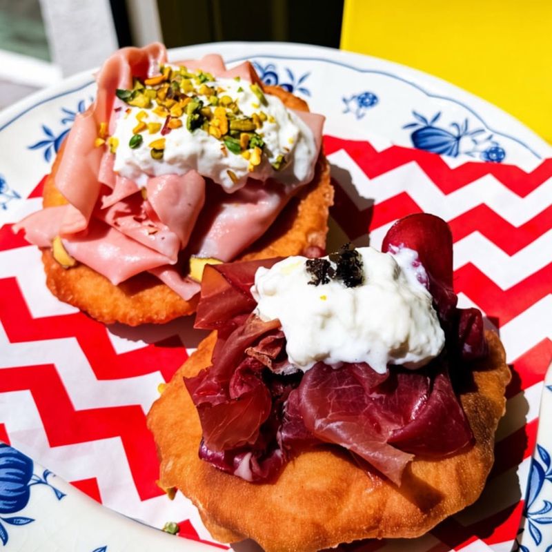 Deux panzerotti ouverts garnis de jambon, de burrata et de pistaches, sur une assiette à motifs