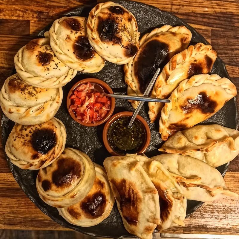 Un plateau d’empanadas dorées autour de deux coupelles de sauce, chimichurri et tomates