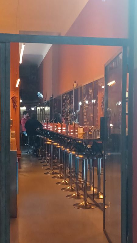 Le long comptoir de Tacos Tacos Tacos, ses tabourets et ses murs orangés, vu depuis la porte