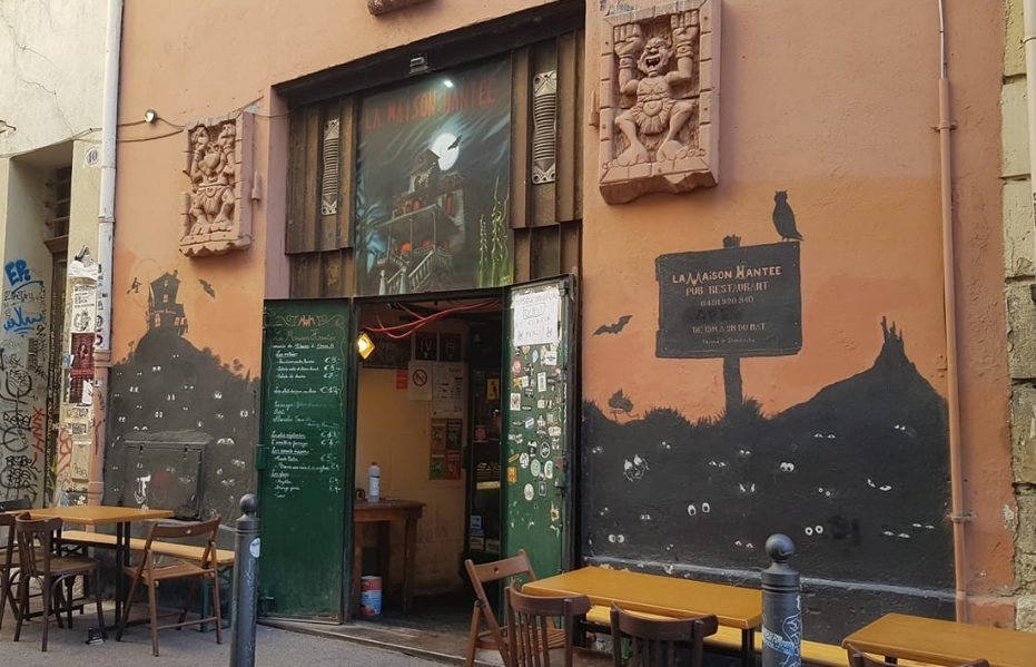 La façade rose de La Maison hantée, rue Vian, avec sa porte en bois et ses masques sculptés