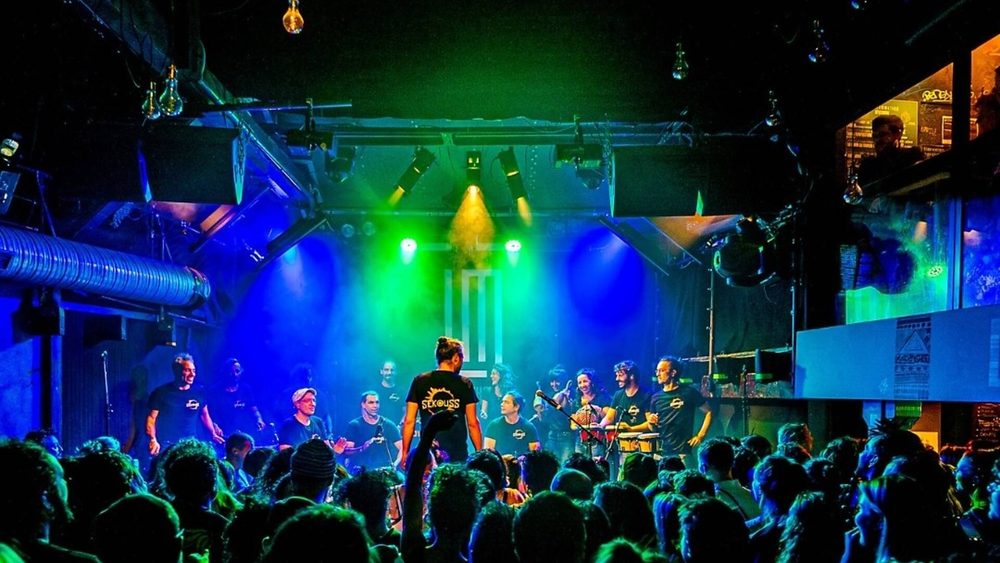 La scène du Makeda baignée de lumières vertes et bleues, devant une salle pleine