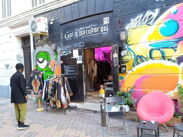 La devanture des 9 salopards, rue Crudère : une enseigne peinte, une fresque colorée et des vêtements exposés sur le trottoir